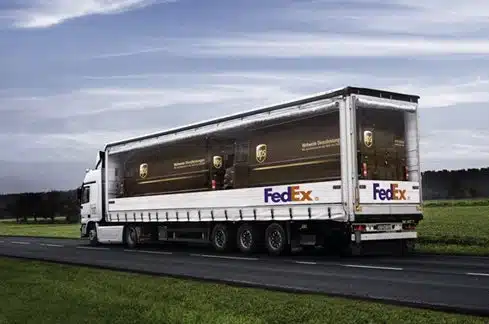 Ciężarówka firmy kurierskiej Fedex z naklejonymi na bokach naklejkami sugerującymi, że w środku znajdują się ciężarówki firmy kurierskiej UPS.